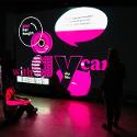 Neon pink, black, and white lights making a display on a screen with a person sitting beside it