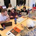 A group of people at a table looking at laptops and a paper with designs on it