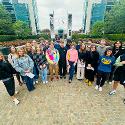 A group of people standing shoulder to shoulder with tall buildings behind them
