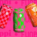Three soda cans with different vibrant designs on them. From left to right: red and pink checkerboard, green and pink wave lines, orange citrus and swirl shapes