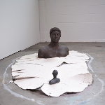 Two female figure busts facing each other emerging from a dried pool of clay on the ground.