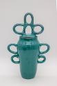 A turquoise colored jar with large circular loop forms for handles on the side and on the lid.