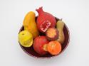 Sculpted ceramic fruits with bites taken out of them resting in a red ceramic bowl.