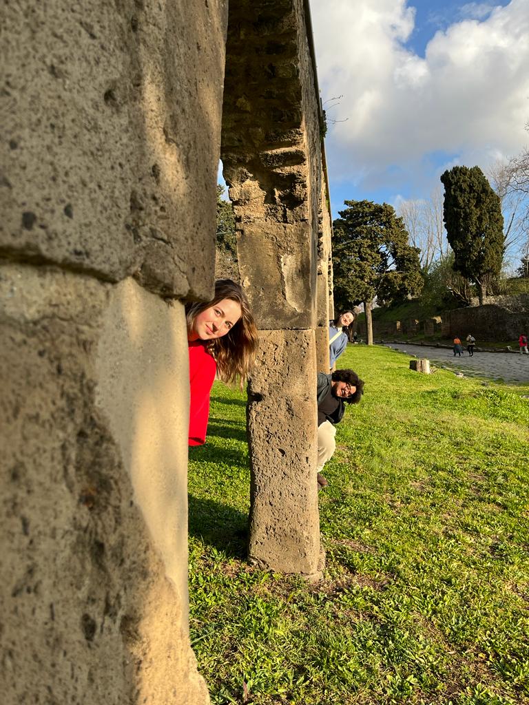 Italy students peaking behind a stone structure 